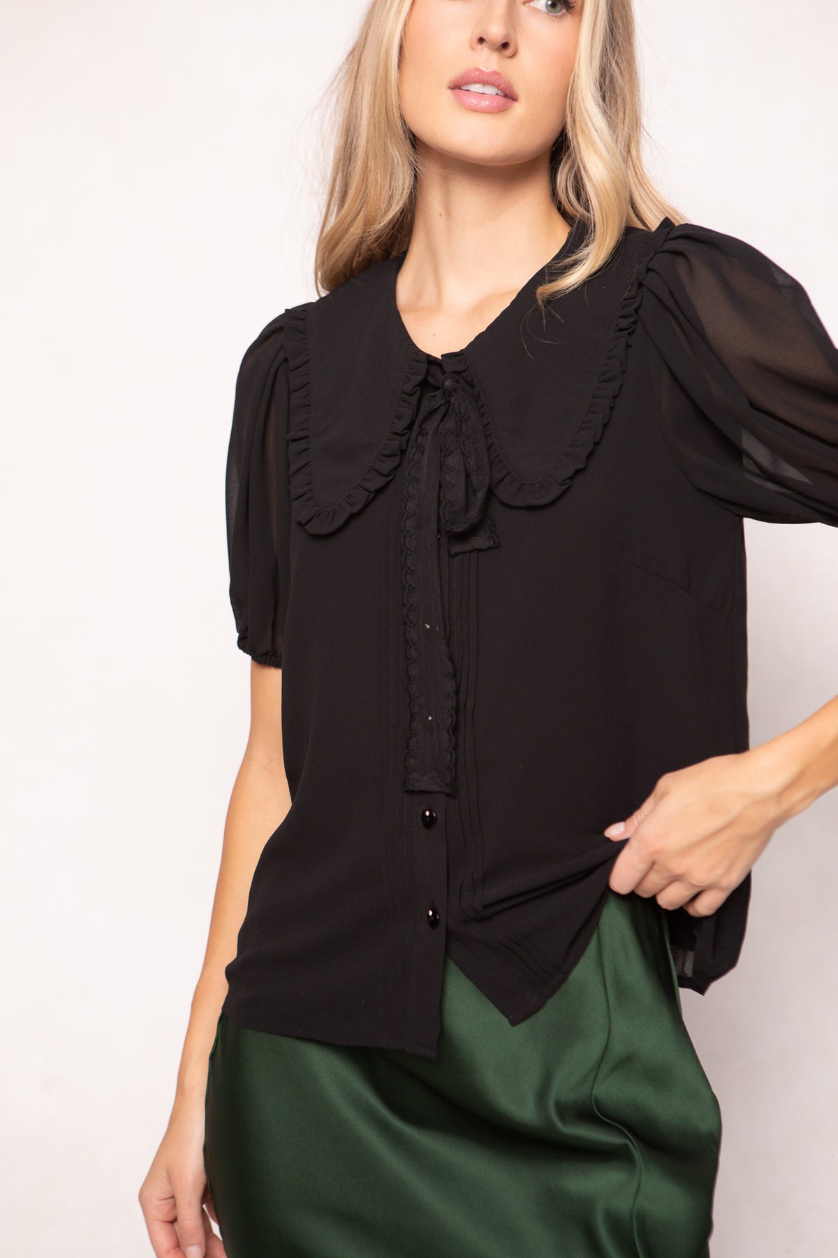 Woman wearing a black blouse with a ruffled collar against a white background