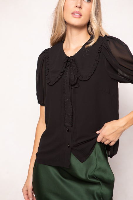 Woman wearing a black blouse with a ruffled collar against a white background