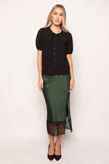 Woman wearing a black blouse with a large collar and a green skirt with lace hem on a white background