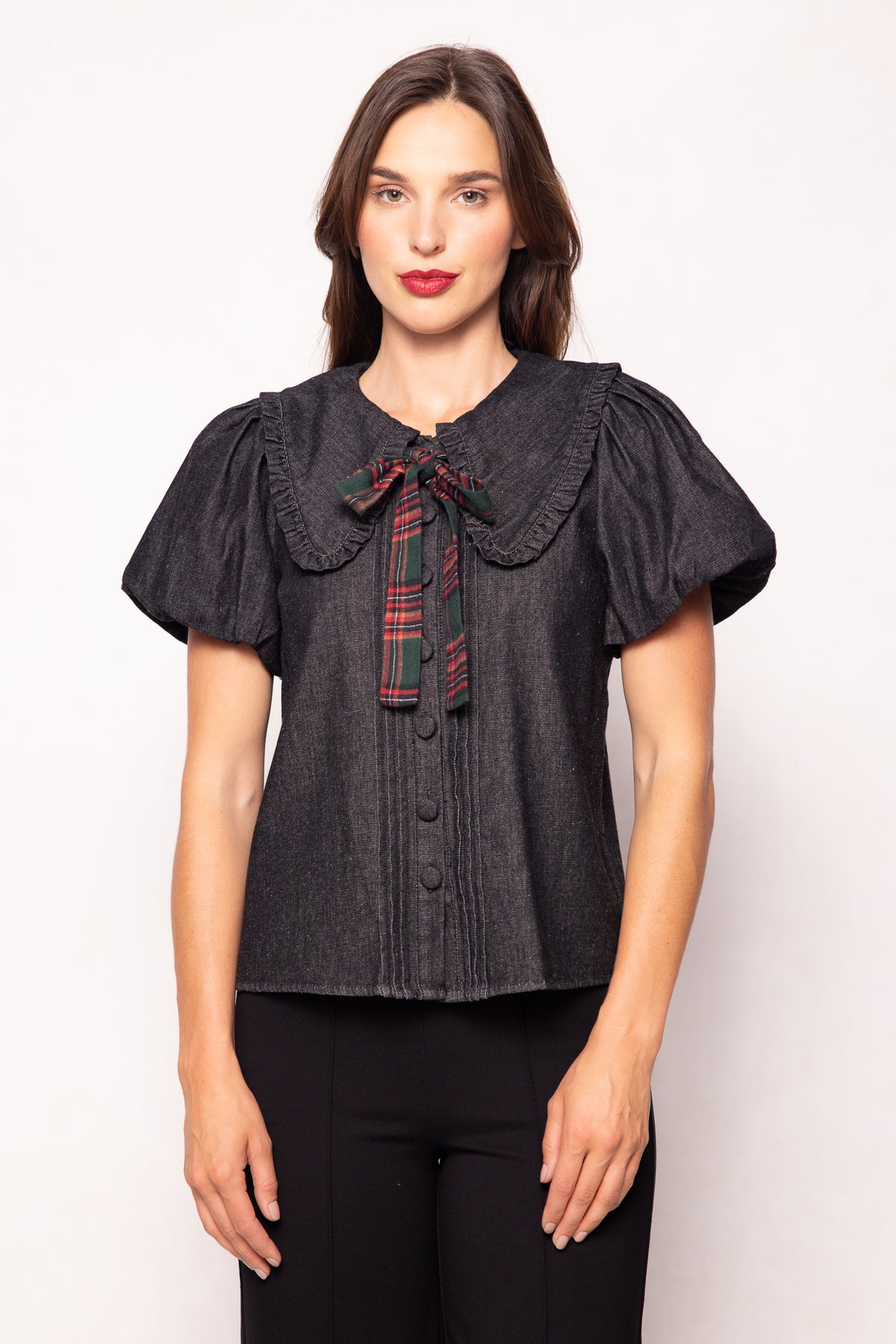 Woman wearing a dark denim blouse with a plaid collar against a white background