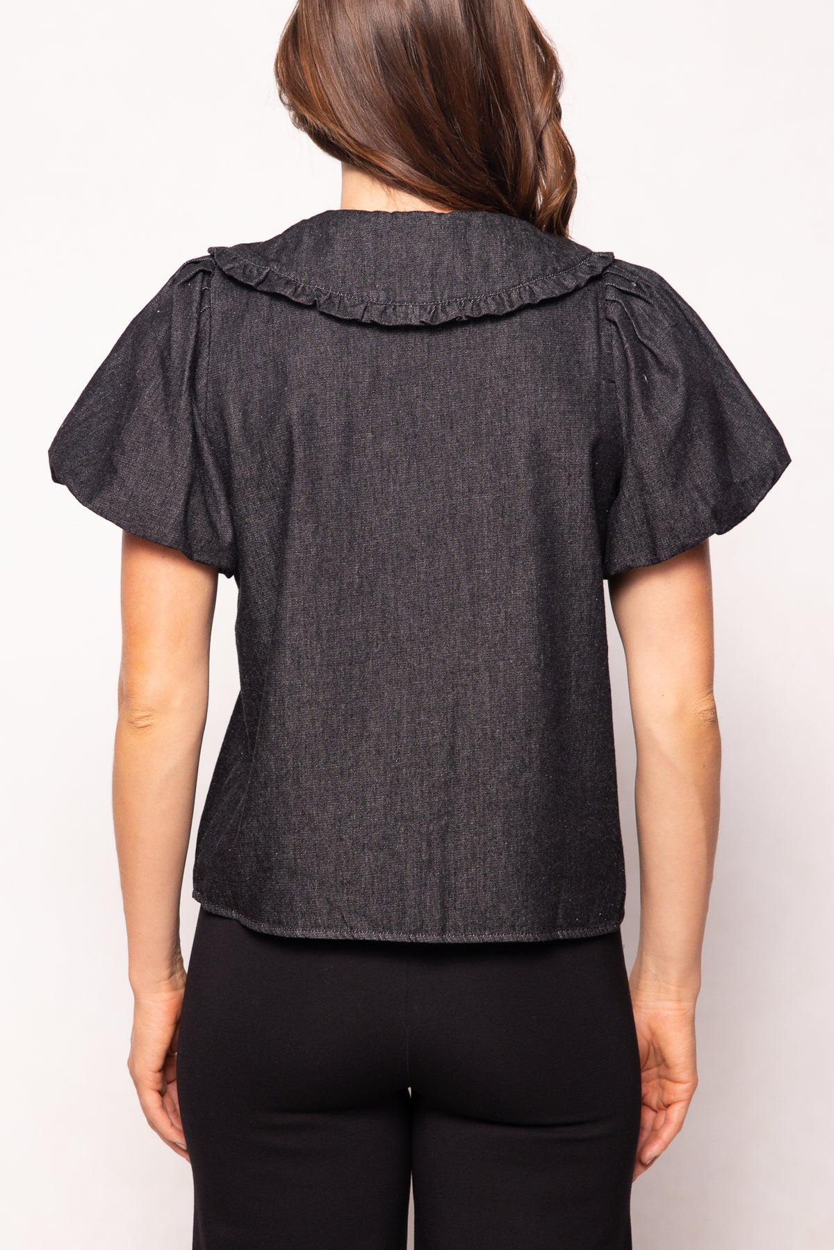 Person wearing a dark denim blouse with ruffled shoulders on a white background