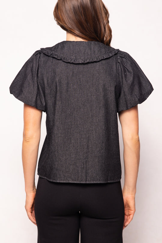 Person wearing a dark denim blouse with ruffled shoulders on a white background