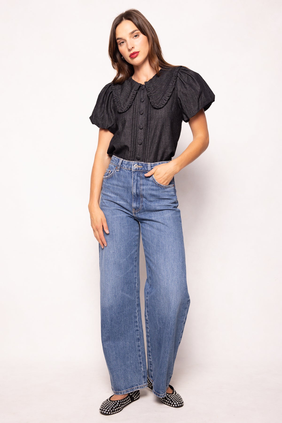 Woman wearing a black blouse with ruffled sleeves and blue jeans on a white background