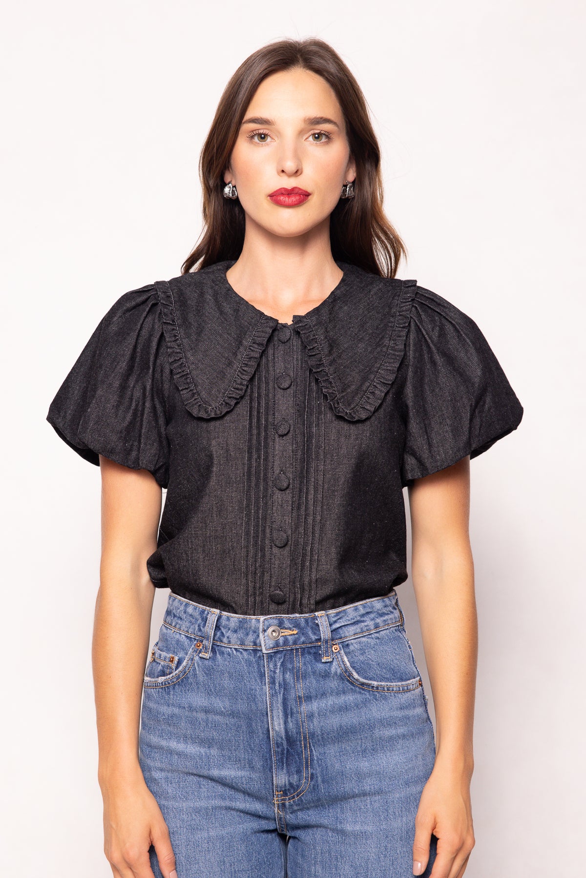 Woman wearing a black blouse with ruffled collar and short sleeves, standing against a white background.