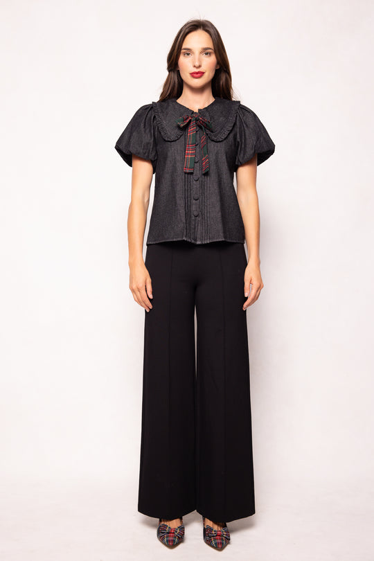 Woman wearing a dark blouse with a plaid collar and black wide-leg pants on a white background