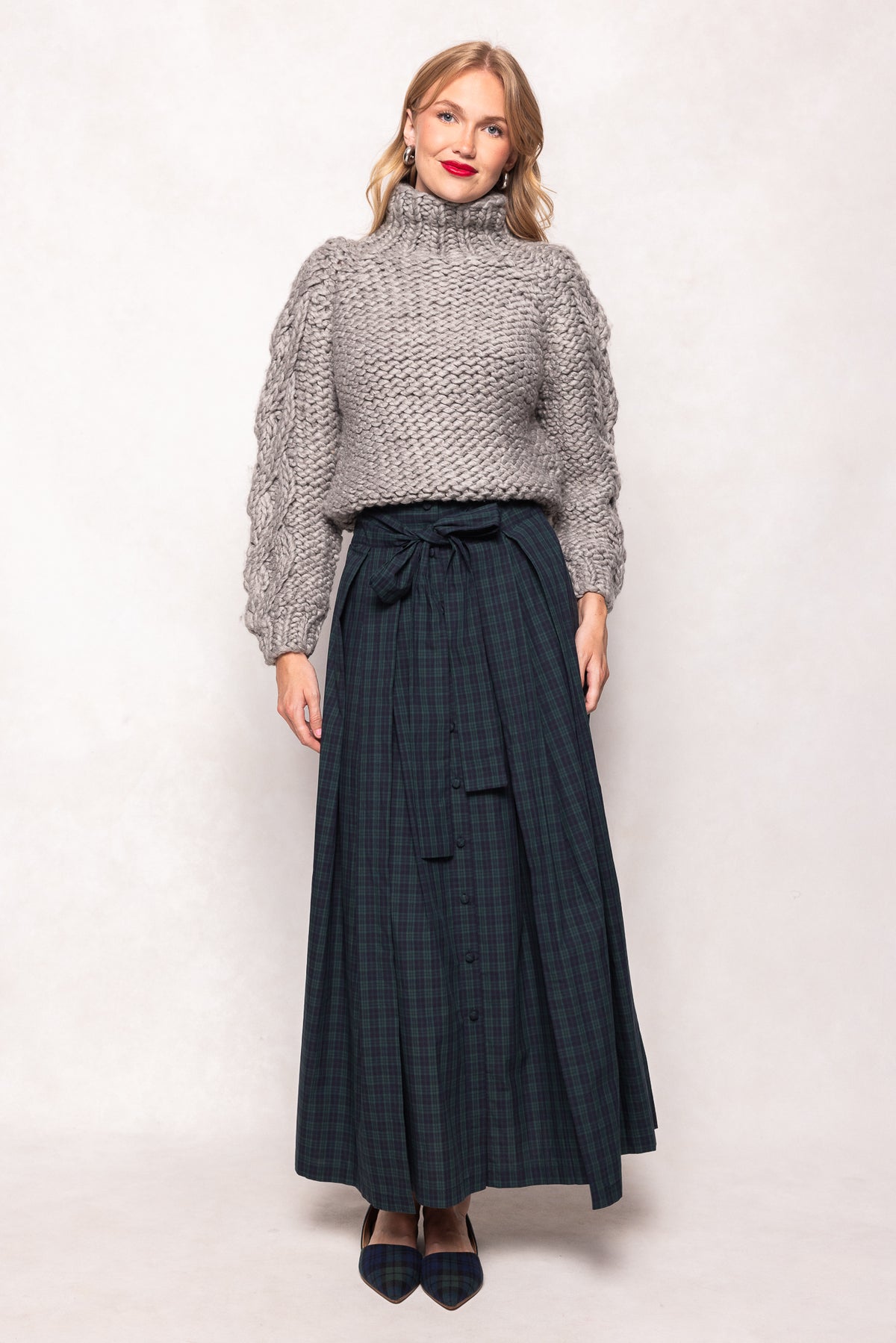 Woman wearing a gray knitted sweater and dark plaid skirt on a white background
