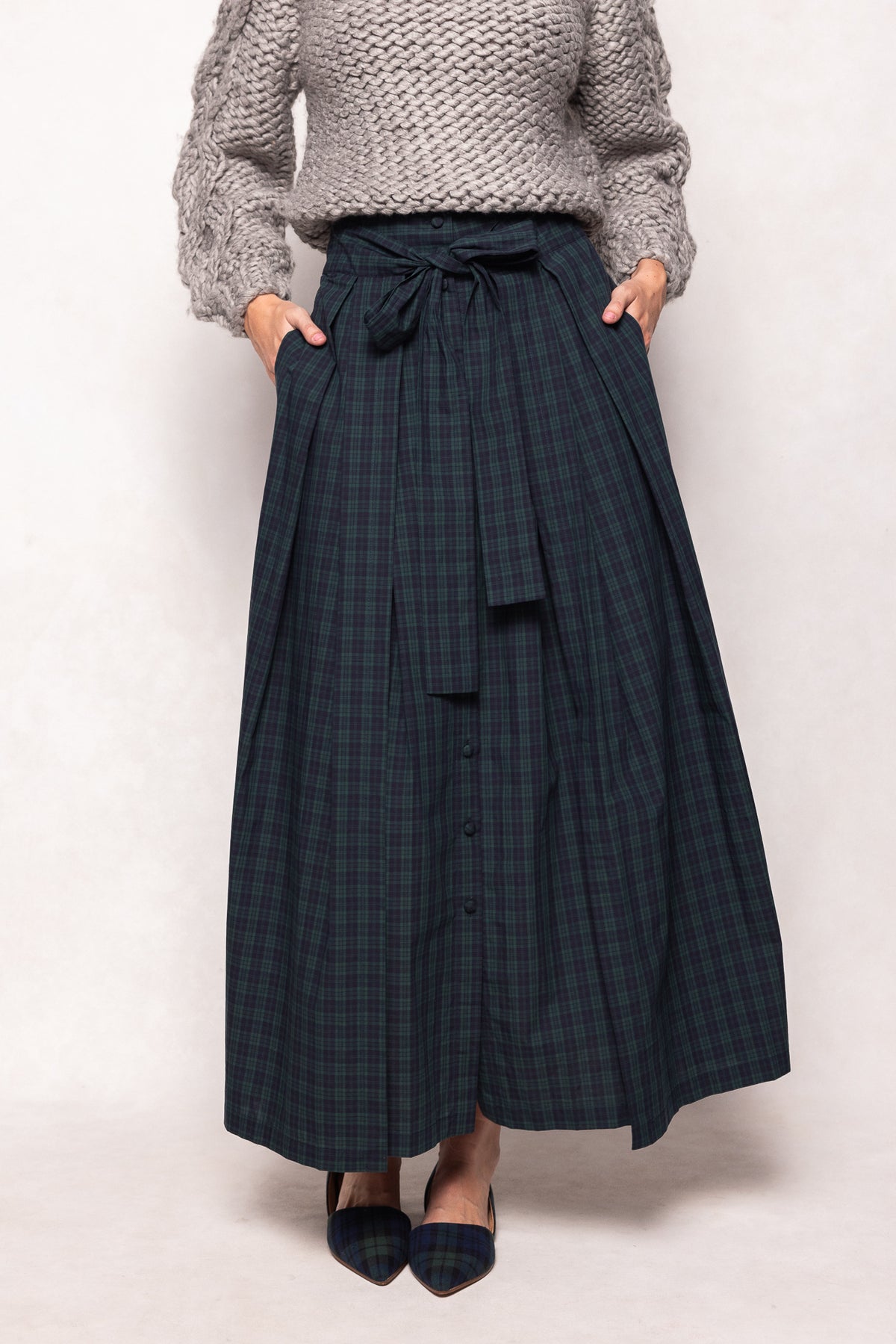 Person wearing a long dark plaid skirt and light gray sweater on a white background