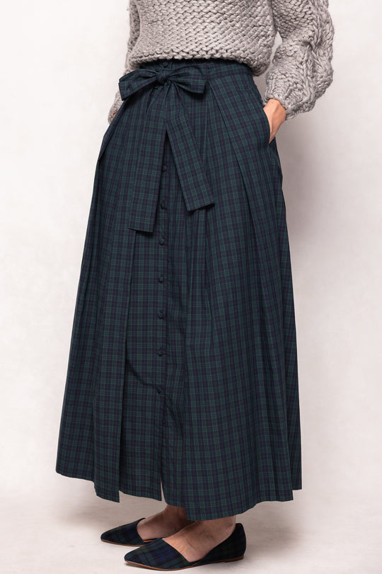 Person wearing a long dark plaid skirt with a white background