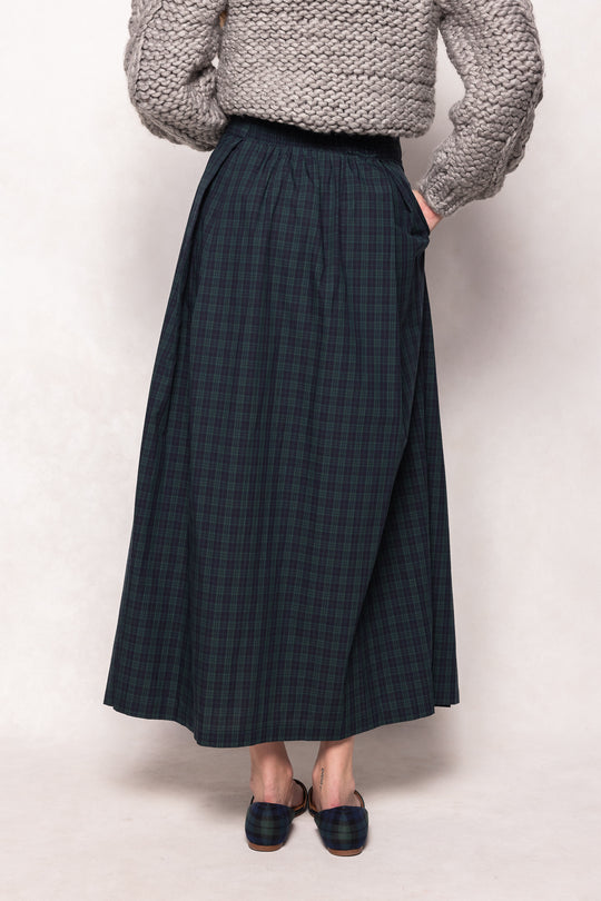 Person wearing a plaid skirt and chunky knit sweater on a plain background