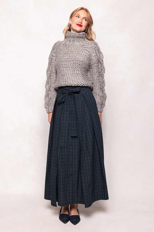 Woman wearing a gray knit sweater and dark plaid skirt on a white background