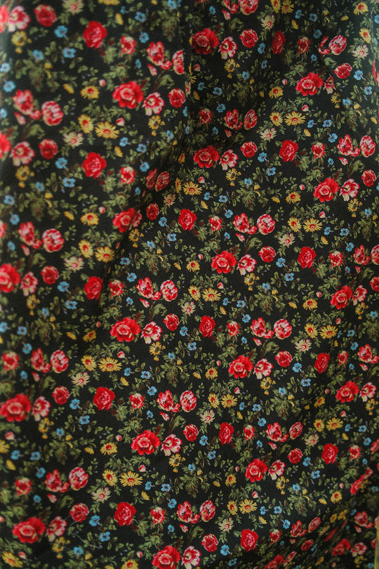 A close-up of the Annalise Dress in Obsidian Vintage Poppies by Ivy City Co, showcasing red, yellow, and blue flowers with green leaves on a dark backdrop.