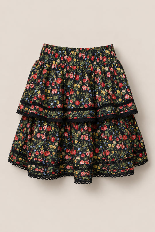 The Annalise Skirt in Obsidian Vintage Poppies by Ivy City Co is a black cotton skirt with red, yellow, and pink floral print, two tiers, a lace-trimmed hem, and shown on a plain beige background.