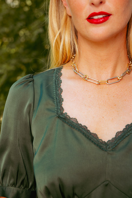 Close-up of a person wearing a green top with lace trim and a gold chain necklace.