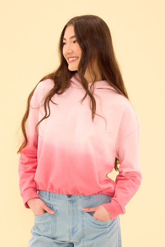 Person wearing a pink and red gradient sweatshirt with a yellow logo on a beige background