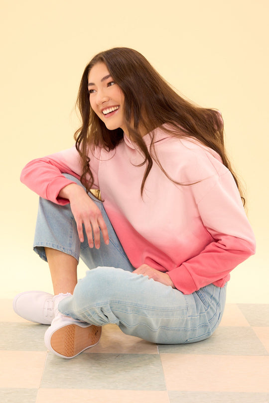 Woman wearing a pink and blue gradient sweater sitting on a light-colored floor.