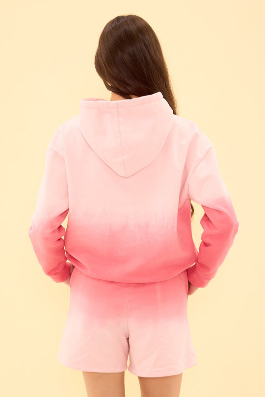Person wearing a pink gradient hoodie and shorts on a beige background
