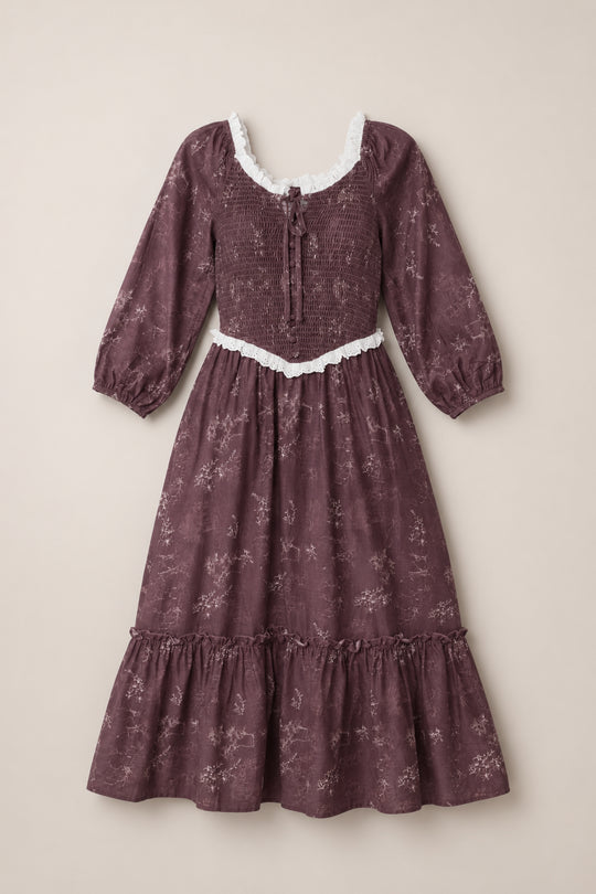 A long-sleeved Asha Dress in Warm Cocoa Valencia Toile by Ivy City Co, featuring a maroon floral pattern with white lace trim, a smocked bodice, ruffled hem, and tie-front neckline, laid flat on a neutral background. This cotton dress is maternity friendly for added comfort and style.