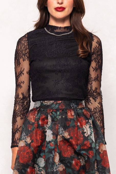 Black lace top with sheer sleeves and a floral skirt on a white background