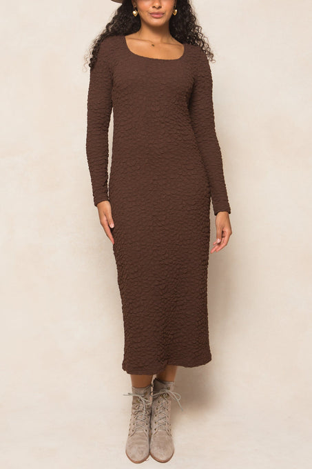 Woman wearing a brown dress and hat against a plain background