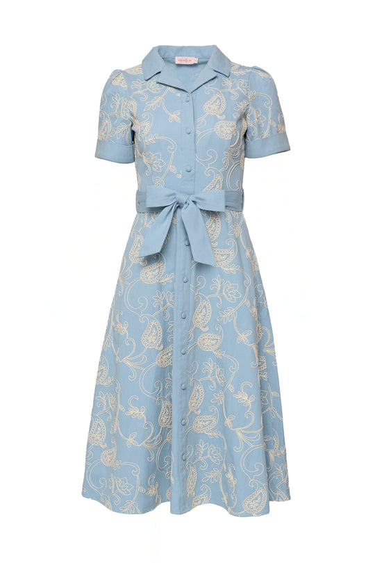 The Ivy City Co Bennett Dress in Cream Embroidery is a short-sleeved chambray denim dress with white floral and paisley patterns, a nursing-friendly button-down front, matching waist tie belt, and vintage-inspired knee-length style.