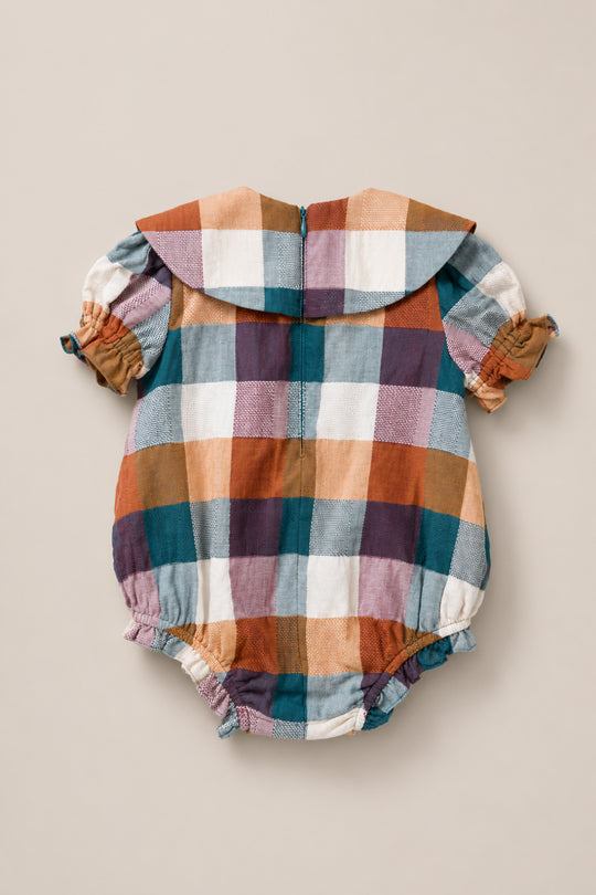 The Ivy City Co Baby Alice Romper in Maize Gingham is a charming cotton-blend romper with a large plaid pattern in blue, orange, brown, and white. It features short puff sleeves, a Peter Pan collar, and elastic leg openings. The garment is displayed flat on a neutral background.