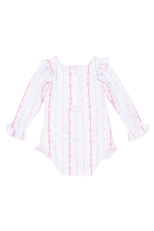 The Ivy City Co Baby Bella Rash Guard in Breea Bow features long sleeves, ruffled cuffs, and a pastel pink and blue bow swimsuit print on white, displayed flat against a white surface.