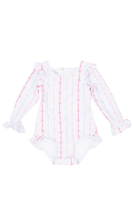 The Ivy City Co Baby Bella Rash Guard in Breea Bow is a long-sleeve romper with ruffled shoulders and cuffs, showcasing a cute pink and blue bow print on white.