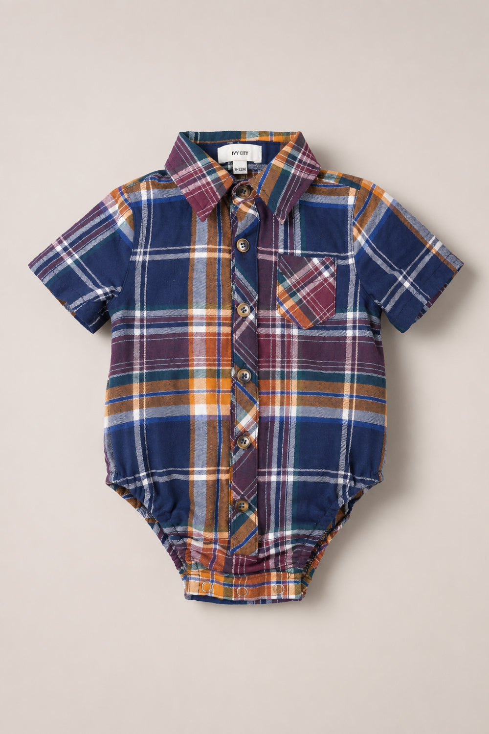 The Ivy City Co Baby Boy James Romper in Midnight Plaid features short sleeves, a multicolored plaid button-down design with front buttons, a collar, and a small chest pocket, displayed laid flat on a neutral background.
