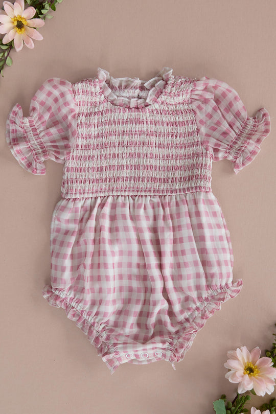 The Ivy City Co Baby Cordelia Romper in Desert Rose Gingham features puffed short sleeves and ruffled edges, shown on a beige background with pink flowers—making it the perfect spring outfit for your little one.