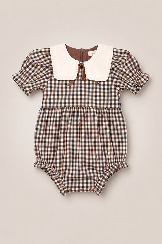 The Baby Emery Romper in Chestnut Gingham by Ivy City Co features a charming brown and white gingham cotton design with short puffed sleeves, ruffled leg openings, and a large white collar. This vintage-inspired romper combines classic style with comfort for your little one and includes a back button closure.