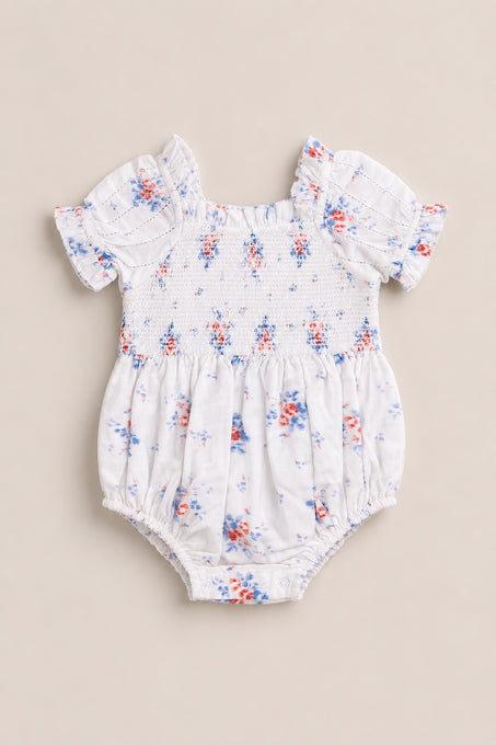 The Ivy City Co Baby Emily Romper in Heritage Soft Ditsy Floral features short puff sleeves, ruffled edges, and a pink and blue ditsy print on white with a smocked bodice. Ideal for adorable mom and me matching looks!.