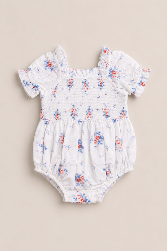 The Ivy City Co Baby Emily Romper in Heritage Soft Ditsy Floral features short puff sleeves, ruffled edges, and a pink and blue ditsy print on white with a smocked bodice. Ideal for adorable mom and me matching looks!.