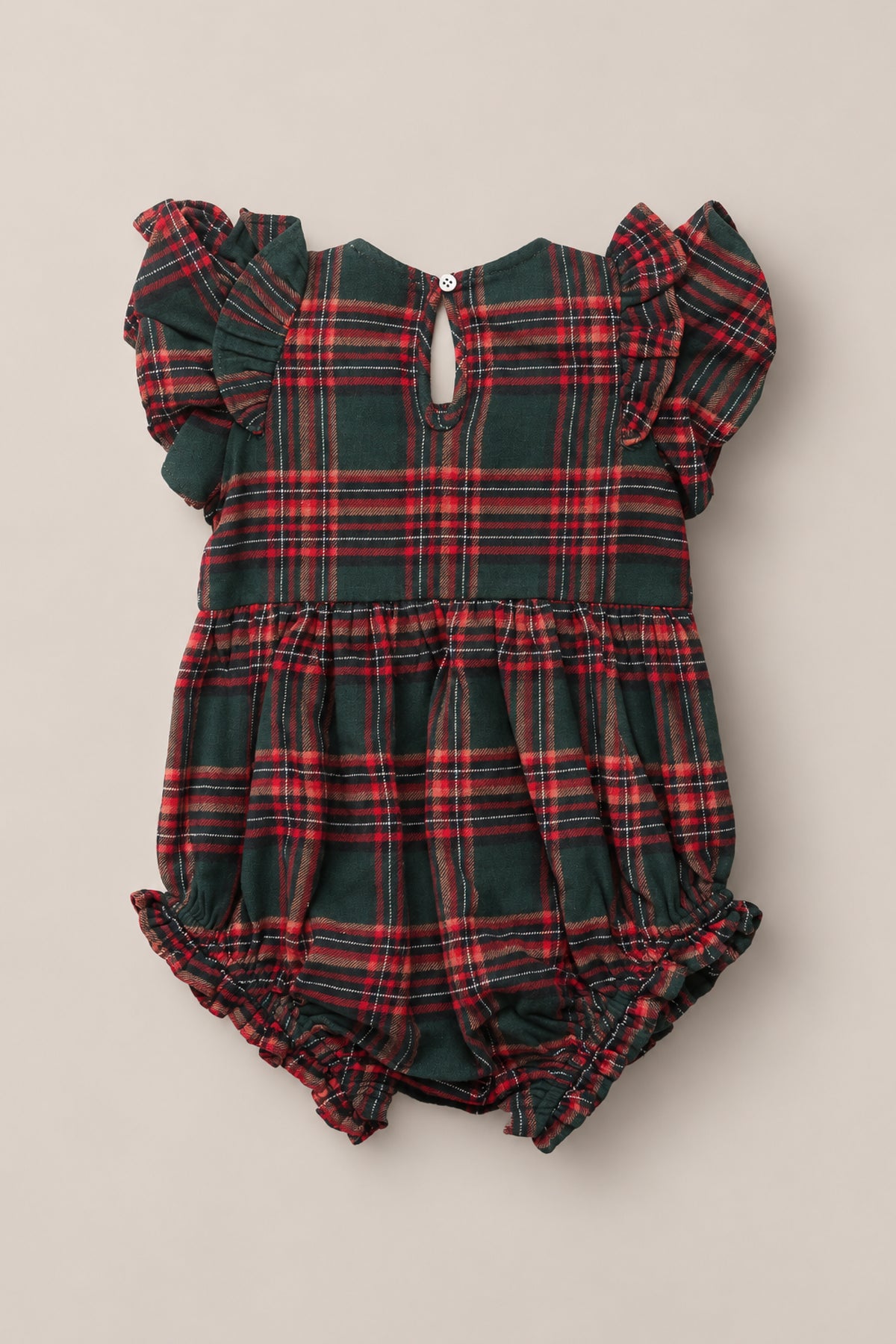 The Baby Hattie Romper in Evergreen Plaid by Ivy City Co is a charming holiday romper featuring a festive red and green plaid print. It has short ruffle sleeves, a gathered waist, and elastic leg openings for added comfort. The back is finished with a small button closure at the neck.