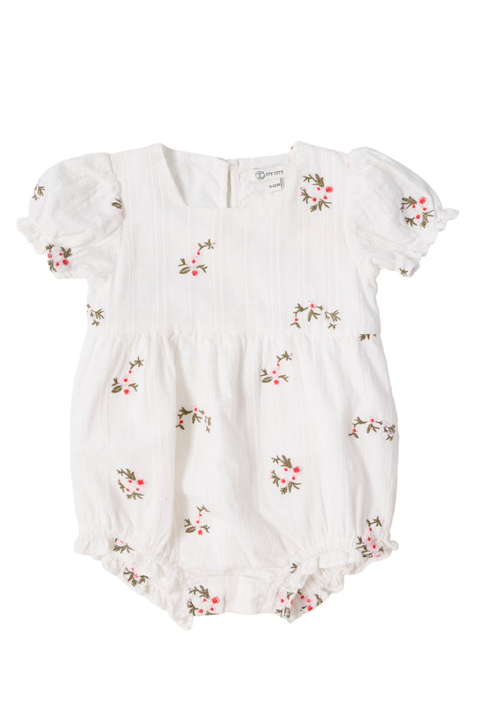 The Ivy City Co Baby Jessie Romper in Ditsy Embroidery is a white cotton romper with pink and green floral embroidery, short puffed sleeves, textured stripes, ruffled legs, gathered waist, smocked bodice, and back buttons.