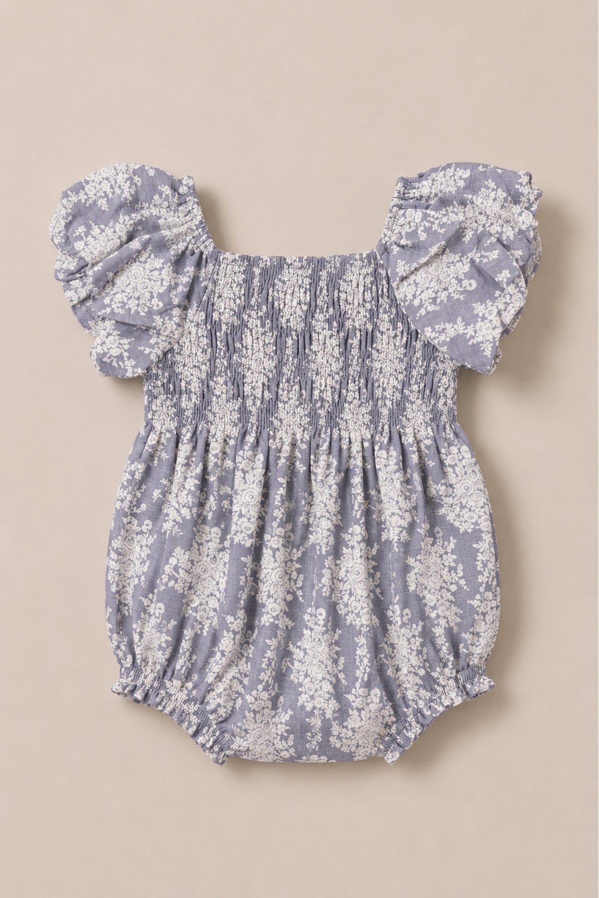 Introducing the Baby Lisa Romper in Jolie Fleur by Ivy City Co, featuring charming puff sleeves, a smocked bodice, and a delicate light purple floral pattern on a beige background.