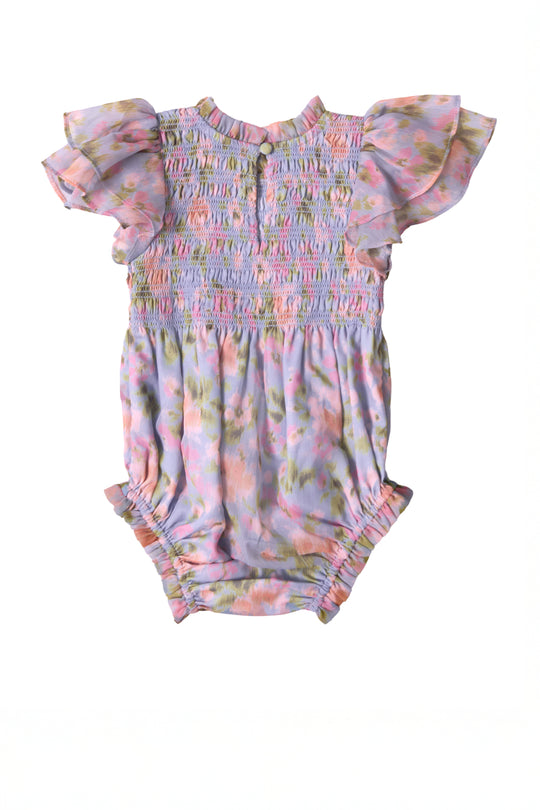The Ivy City Co Baby Lottie Romper in Vibrant English Garden features ruffled flutter sleeves, a smocked bodice, gathered leg openings, and a pastel floral print with pink, purple, green, and yellow tones.