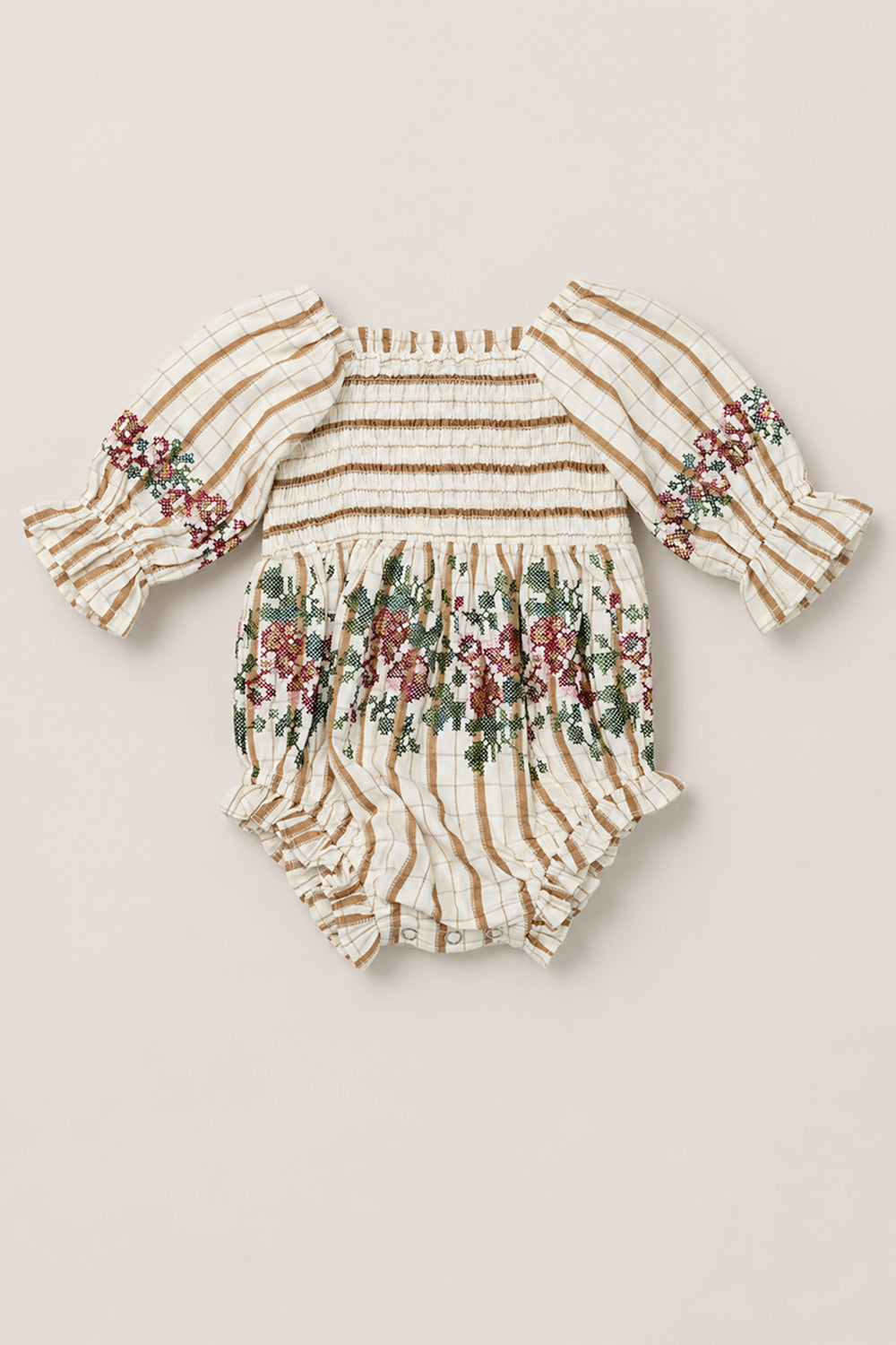 The Baby Madeline Romper in Embroidered Cider Grid by Ivy City Co is an adorable cotton-blend romper in a cream and tan grid pattern, highlighted by intricate floral embroidery, a smocked bodice, sweet puff sleeves with ruffle cuffs, and a cozy bloomer bottom with handy snap closures.