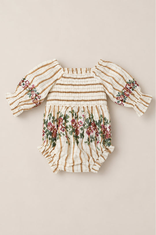 The Baby Madeline Romper in Embroidered Cider Grid by Ivy City Co is a charming cotton-blend romper with long sleeves, showcasing a beige and white grid pattern, a delicately smocked bodice, and floral embroidery on the sleeves and around the waist.