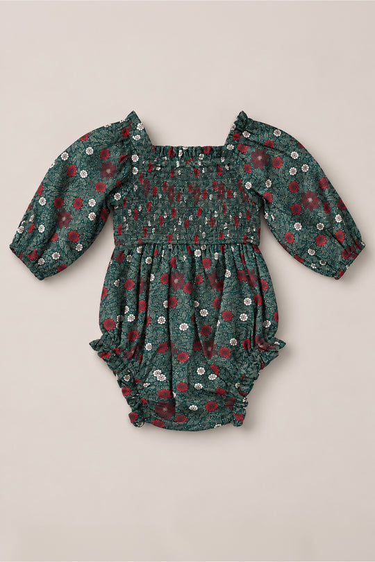 The Ivy City Co Baby Madeline Romper in Evergreen Merry Ditsy features a green base with a charming red and white floral pattern, smocked bodice, square neckline, and gathered ruffle leg openings. Crafted from 100% cotton, this long-sleeve girls’ Christmas romper is perfect for holiday celebrations and cozy days alike, shown laid flat on a light background.