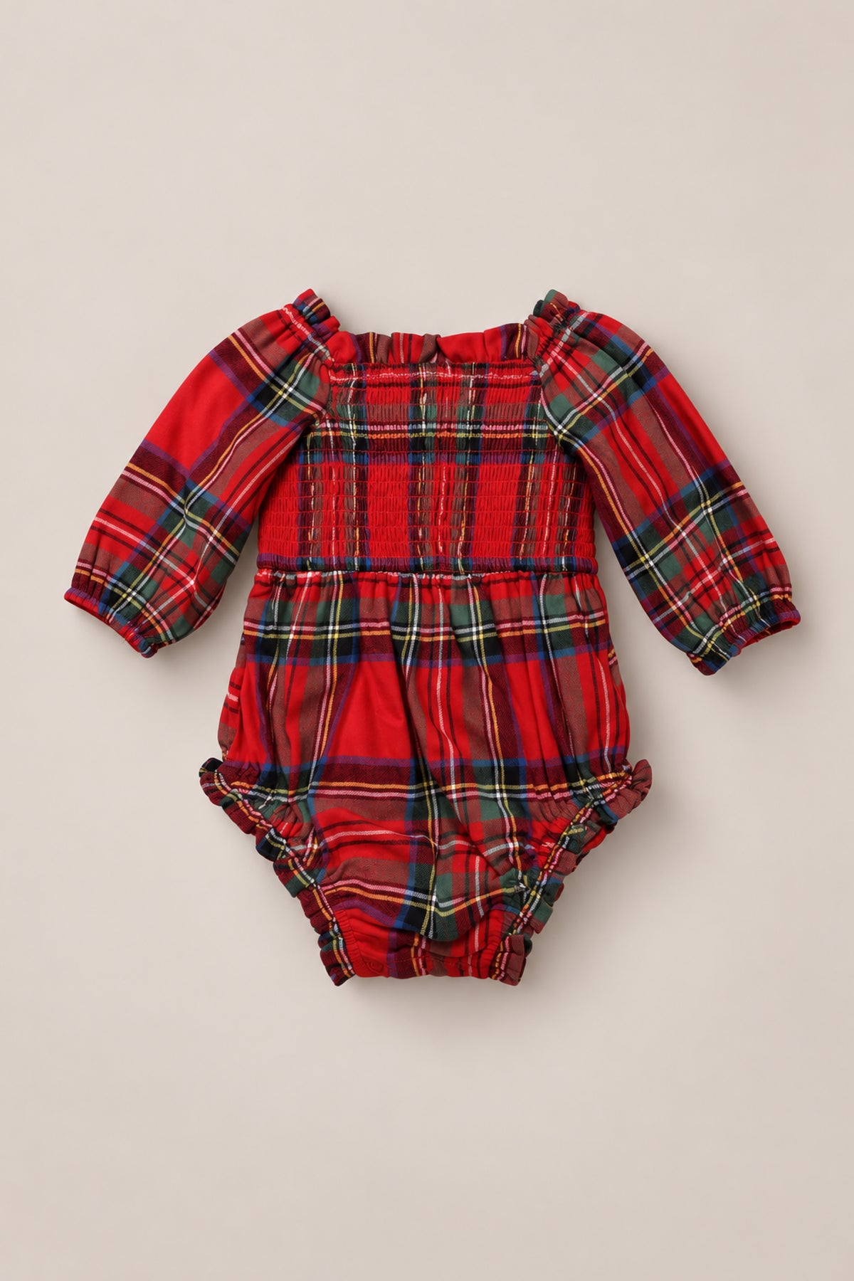 The Ivy City Co Baby Madeline Romper in Holiday Plaid is a long-sleeve baby romper with a vibrant red, green, yellow, and blue plaid pattern, featuring a smocked bodice and ruffled neckline—perfect for festive holiday outfits—shown against a neutral background.