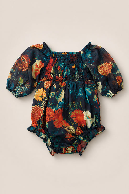 The Baby Madeline Romper in Imogen Moody Floral by Ivy City Co is a charming baby romper with puffed short sleeves and a smocked bodice, showcasing a vibrant orange, red, and green botanical pattern on a dark background. Crafted from chiffon, this delightful romper blends comfort and style for your little one.