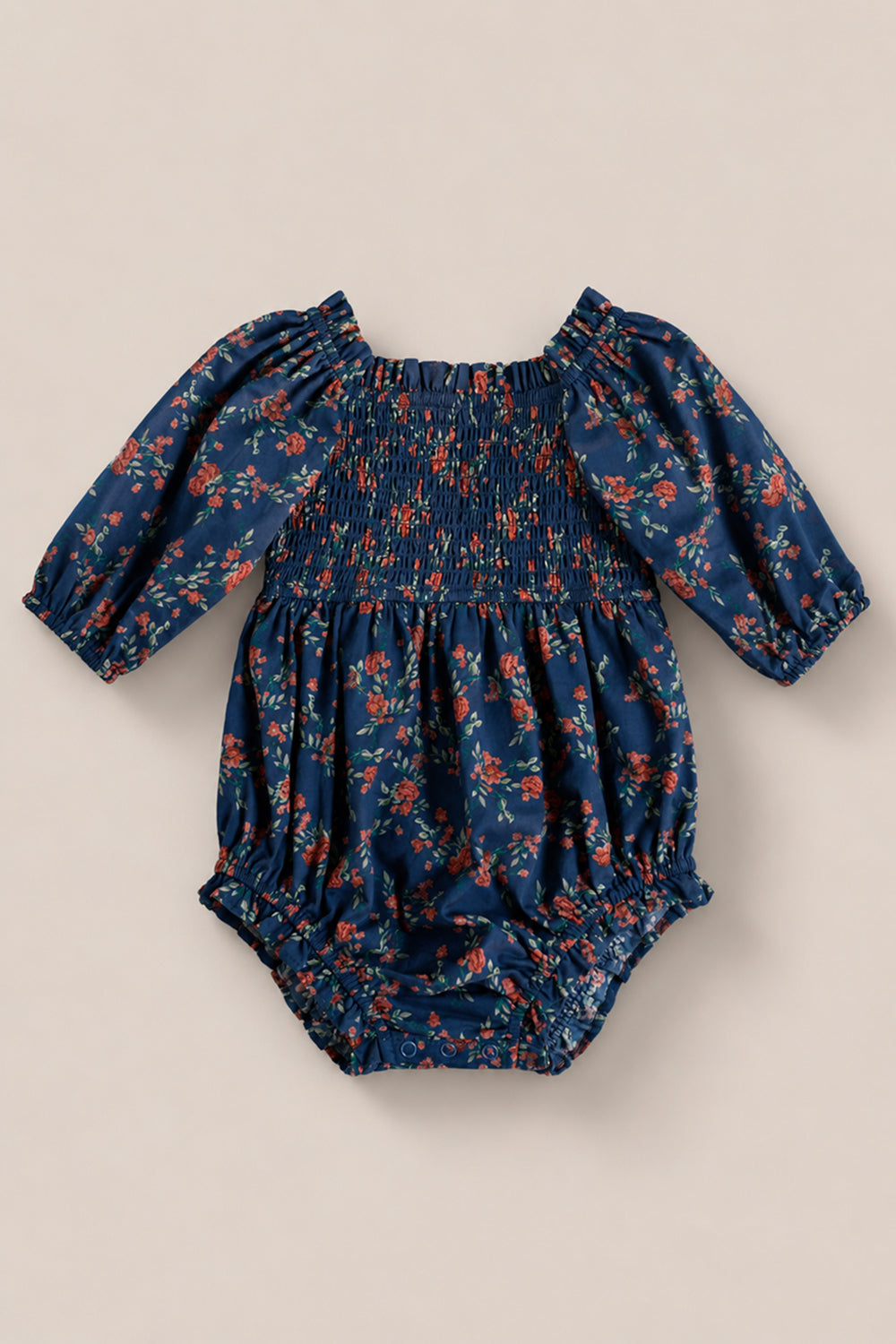 The Ivy City Co Baby Madeline Romper in Midnight Vibrant Chintz features a smocked bodice, red and orange floral print, elastic cuffs and leg openings, shown on a plain beige background.