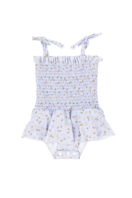 The Ivy City Co Baby Maggie One Piece in Blue Ditsy Floral features shoulder tie straps, a smocked bodice, ruffled peplum skirt, yellow flowers, and crotch snap buttons for easy diaper changes.