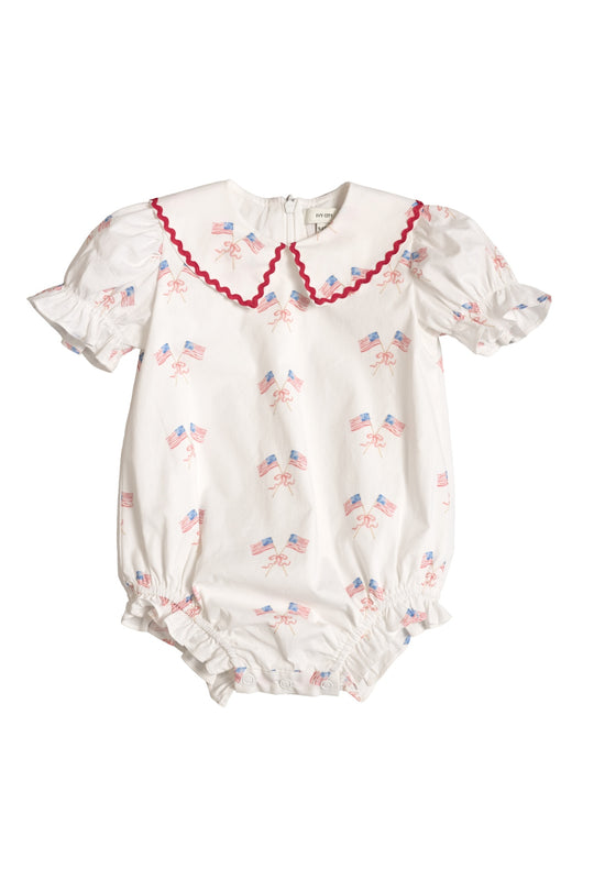 The Ivy City Co Baby Maisy Romper in Star Spangled features ruffled short sleeves, a scalloped red-trimmed collar, American flag bows, gathered leg openings, and a back zipper—perfectly patriotic for your baby girl’s Fourth of July look.