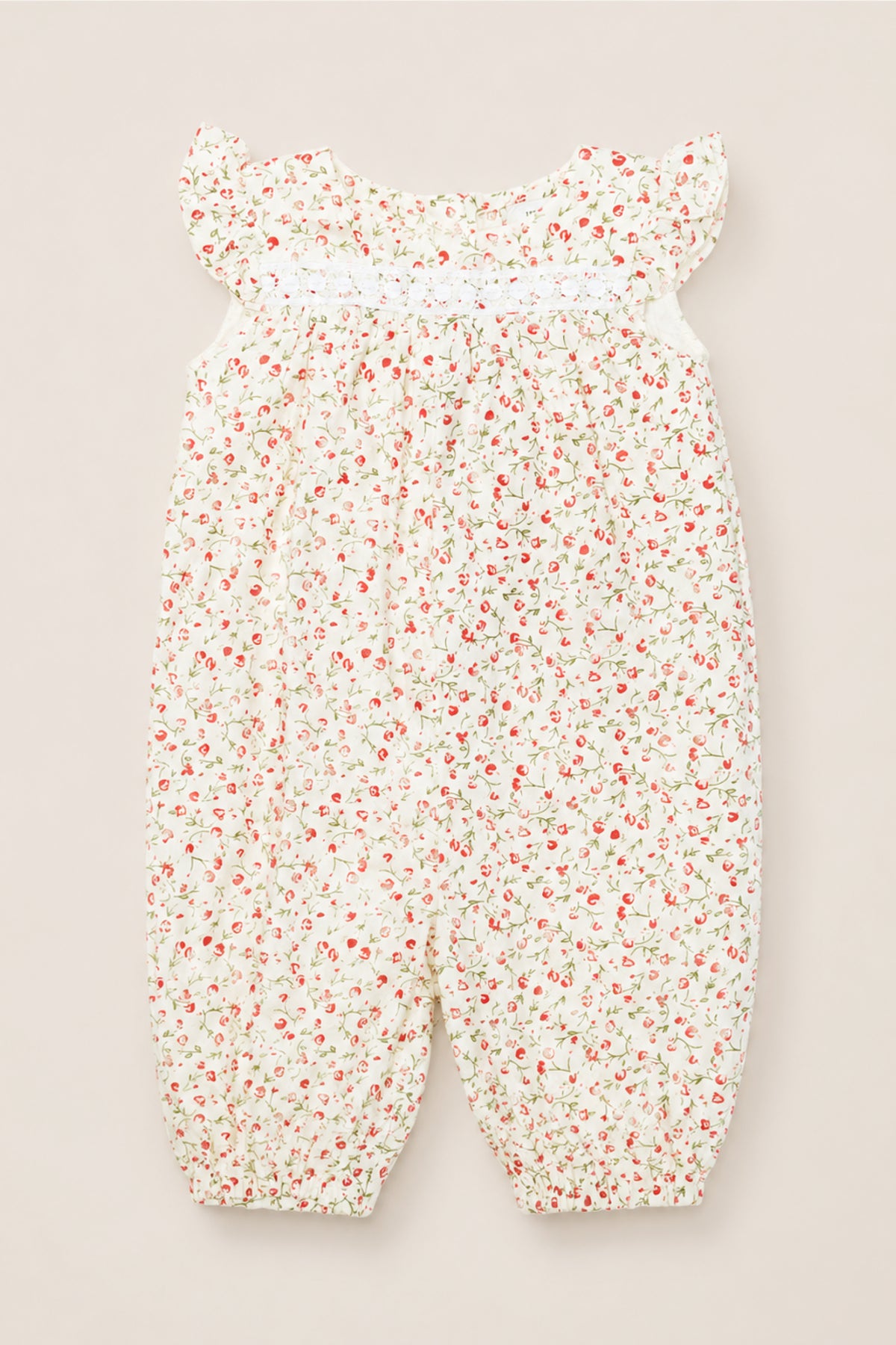 The Ivy City Co Baby Mirabelle Romper in Cream Ditsy Floral features short ruffle sleeves, a gathered neckline, and a white background adorned with a delicate red and green floral print. Crafted from soft cotton, this charming romper is finished with lace trim for an extra touch of sweetness.