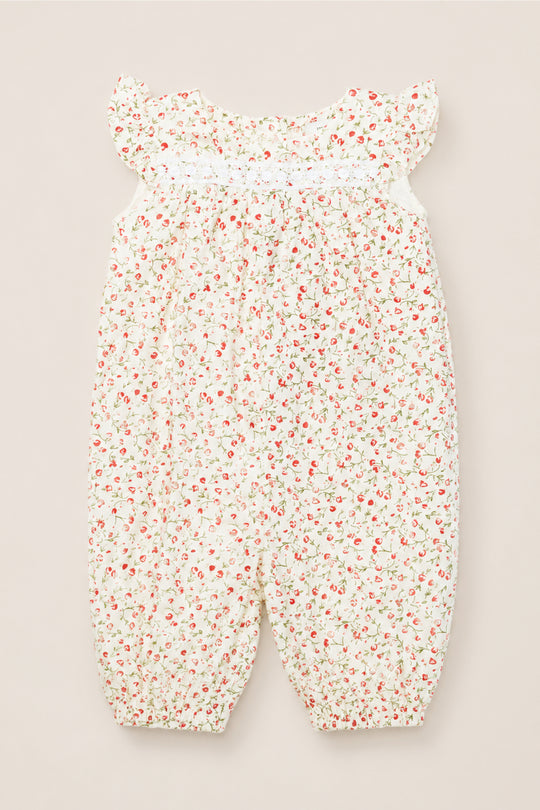 The Ivy City Co Baby Mirabelle Romper in Cream Ditsy Floral features short ruffle sleeves, a gathered neckline, and a white background adorned with a delicate red and green floral print. Crafted from soft cotton, this charming romper is finished with lace trim for an extra touch of sweetness.
