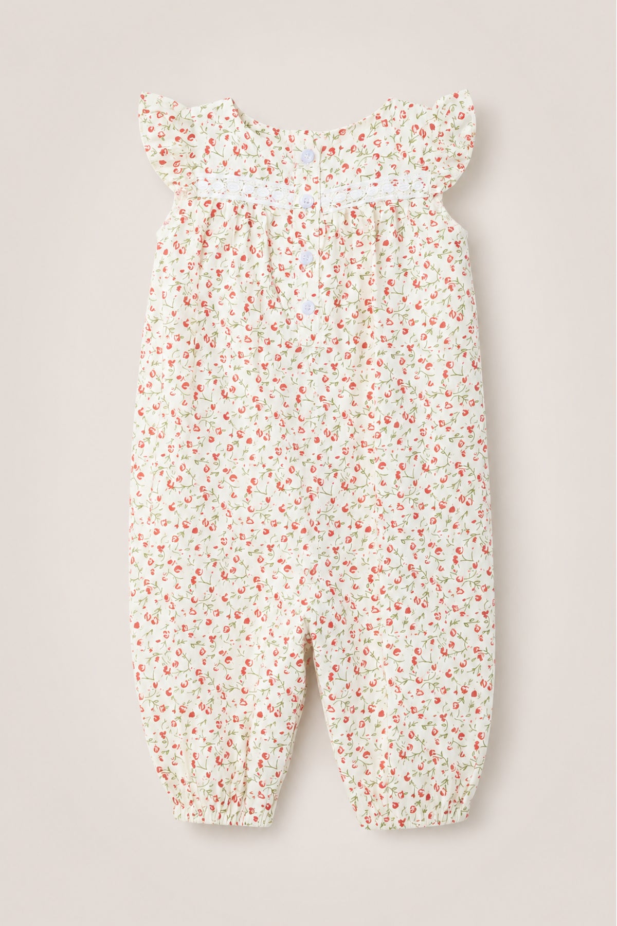 The Ivy City Co Baby Mirabelle Romper in Cream Ditsy Floral showcases a delicate red and pink floral print on a white background. Designed with short flutter sleeves and a smocked chest, this soft cotton romper features gathered ankle cuffs for a loose, comfortable fit. A subtle lace trim adds an extra touch of sweetness to this adorable piece, pictured flat on a neutral surface.