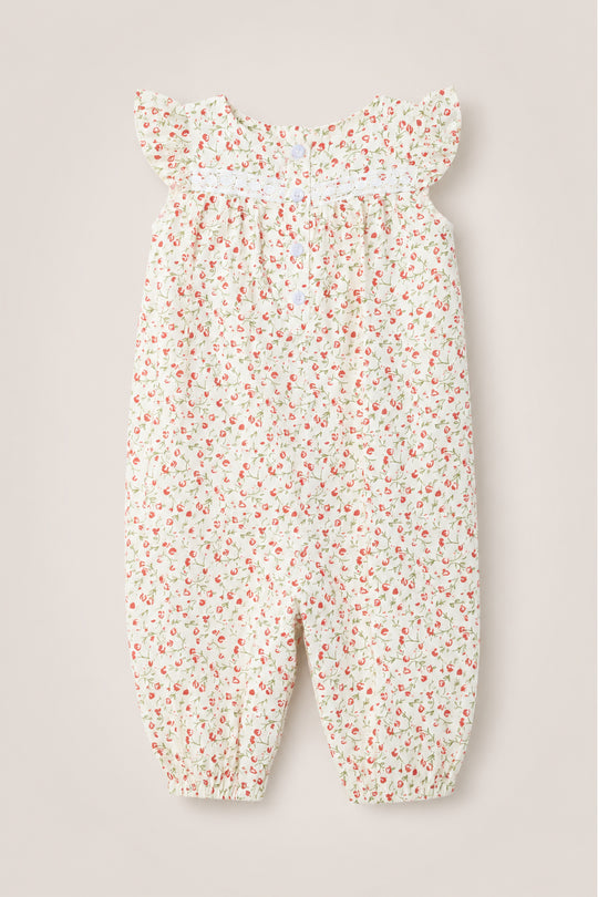 The Ivy City Co Baby Mirabelle Romper in Cream Ditsy Floral showcases a delicate red and pink floral print on a white background. Designed with short flutter sleeves and a smocked chest, this soft cotton romper features gathered ankle cuffs for a loose, comfortable fit. A subtle lace trim adds an extra touch of sweetness to this adorable piece, pictured flat on a neutral surface.