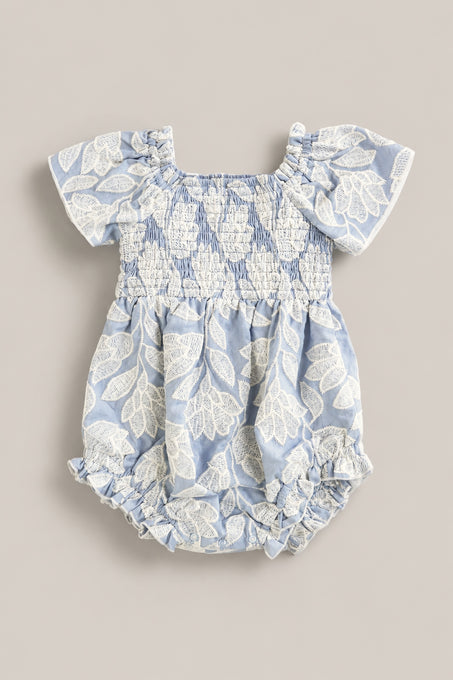 The Ivy City Co Baby Ophelia Romper in Mosaic Embroidery features light blue fabric, short sleeves, white leaf embroidery, smocked chest and waist, and ruffled leg openings for a soft Mom and Me matching look.