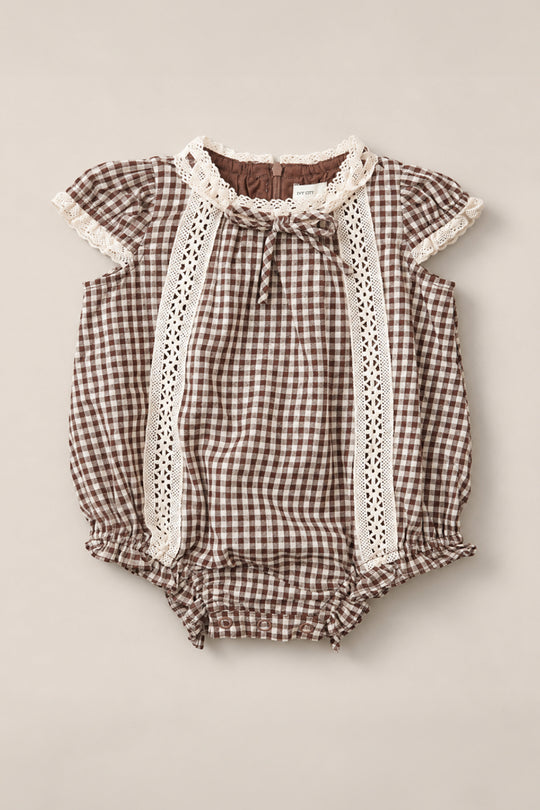 The Ivy City Co Baby Palermo Romper in Hickory Gingham, featuring white lace trim, short puff sleeves, and ruffled leg openings, is laid flat on a neutral background. This charming cotton-blend romper is perfect for any occasion.